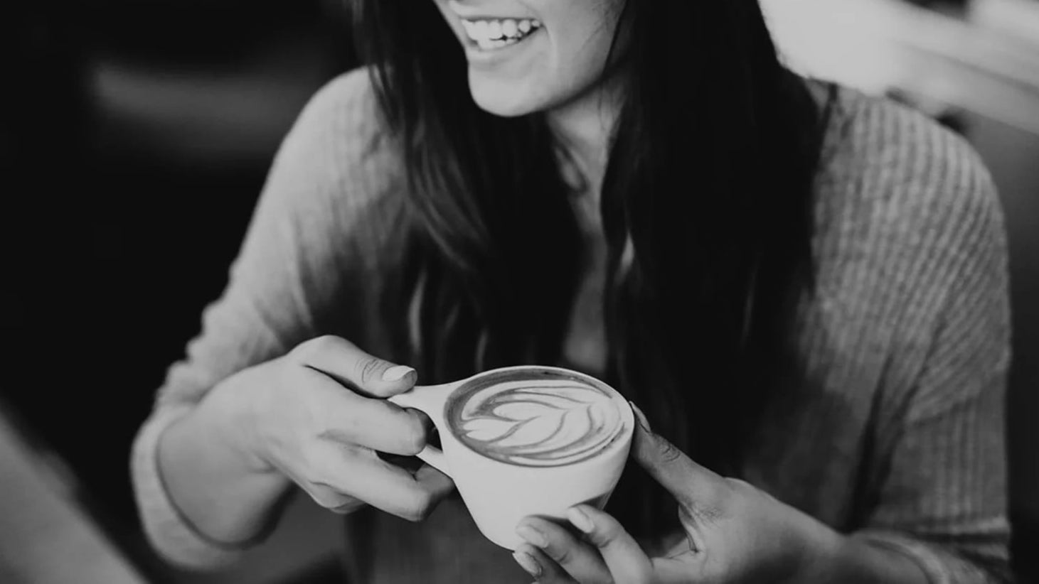Person holding a cup with a latte art design in a black and white setting
